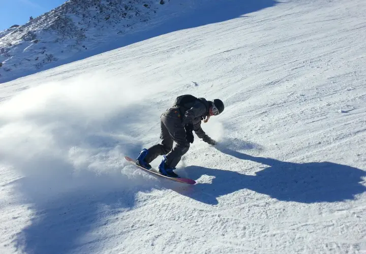 Snowboardzista w akcji na stoku, tworząc obłok śniegu. Idealne **deski do freeride** pozwalają na takie ewolucje.