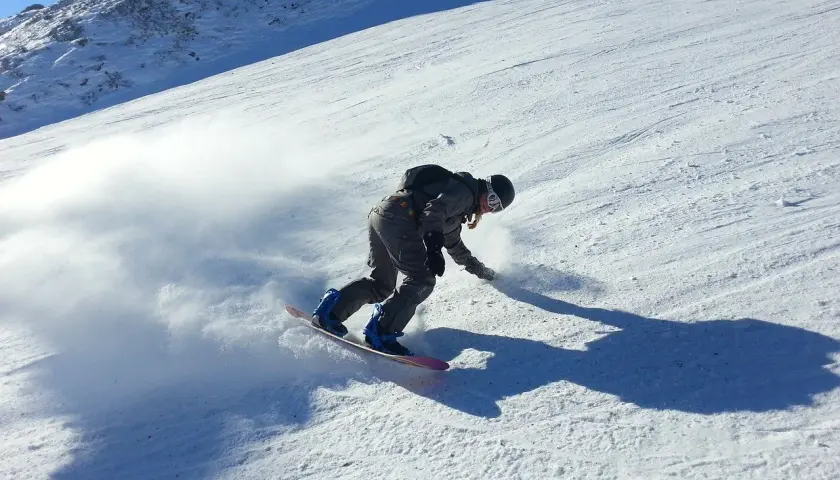 Snowboardzista w akcji na stoku, tworząc obłok śniegu. Idealne **deski do freeride** pozwalają na takie ewolucje.
