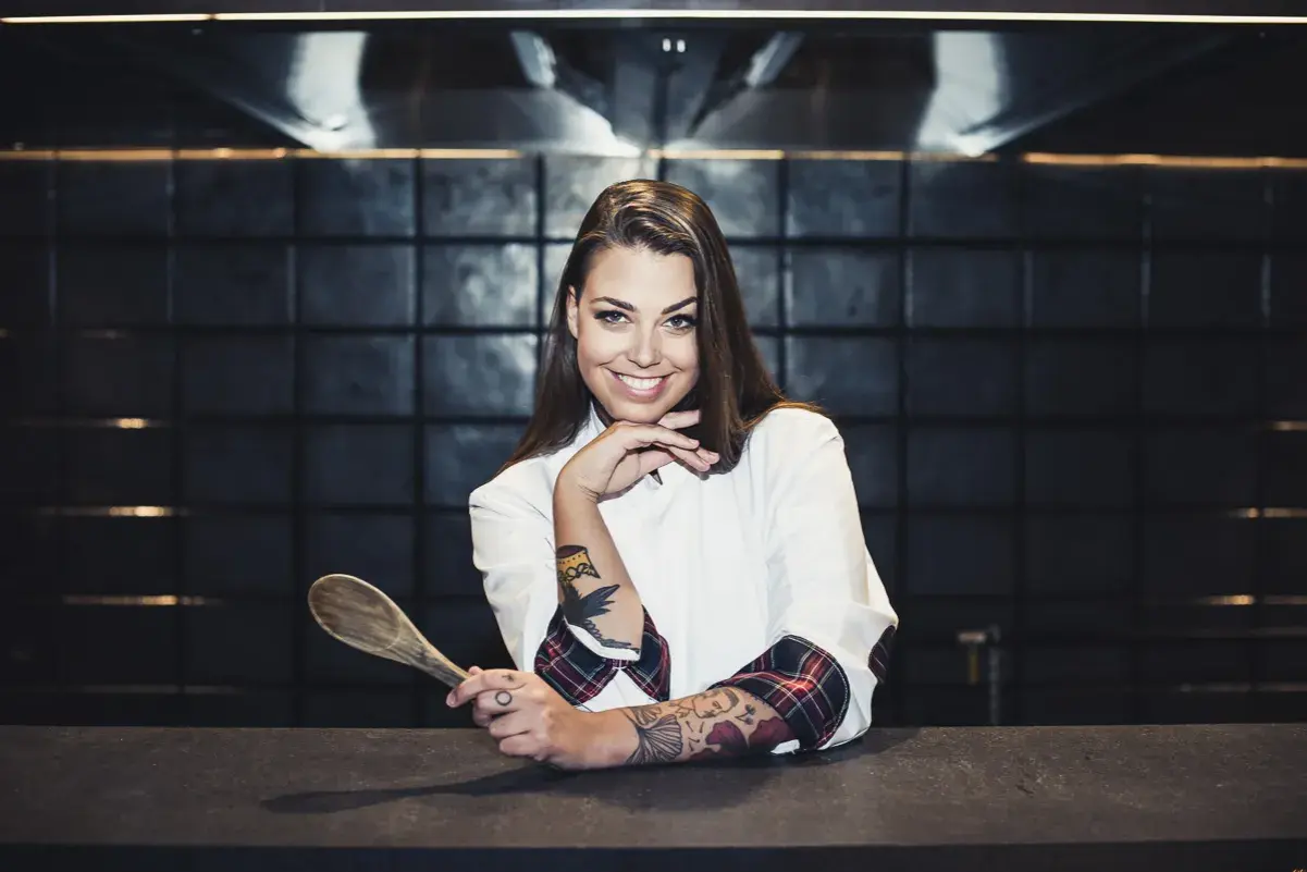 Adriana Marczewska, młoda kucharka z tatuażami, trzyma drewnianą łyżkę.