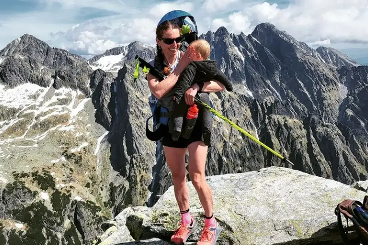 Justyna Kowalczyk z dzieckiem na szczycie górskim, w tle majestatyczne Tatry.