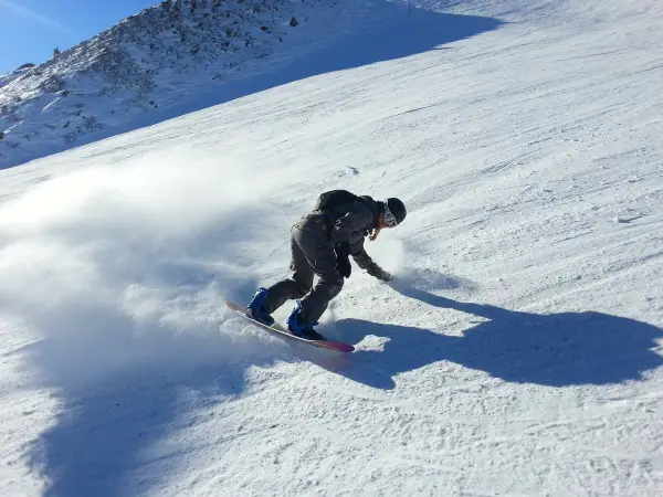 Snowboardzista w akcji na stoku, tworząc obłok śniegu. Idealne **deski do freeride** pozwalają na takie ewolucje.